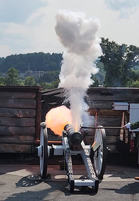 A cannon firing from a rooftop in a gout of orange flame and gray smoke