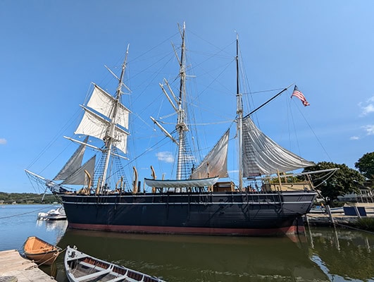 An ol 3-masted sailing ship floats on the water on a cloudless day