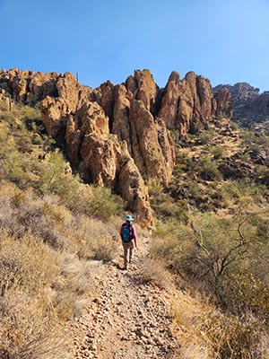 A woman hikes down a trail toward a rocky outcropping on a hill