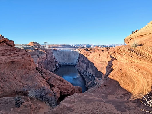 A large concrete dam blocks one end of a large red rock canyon