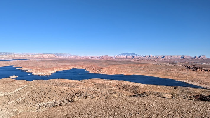 The blue waters of Lake Powell lie below with red rock formations and desert beyond