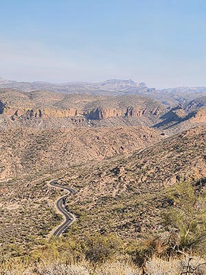 A 2-lane road winds through a valley floor with desert mountains rising above it