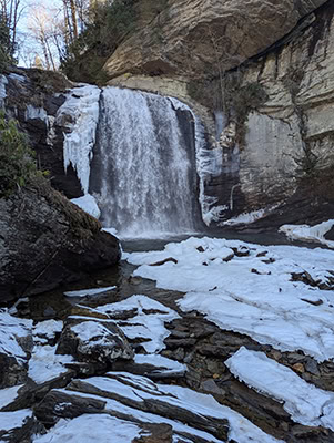 A waterfall with ice along the edges and snow on the rocks in the plunge pool