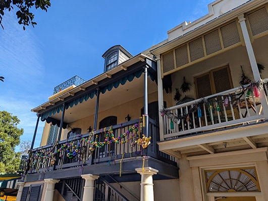 A second floor balcony with iron-work railings draped with green, gold, and purple beads