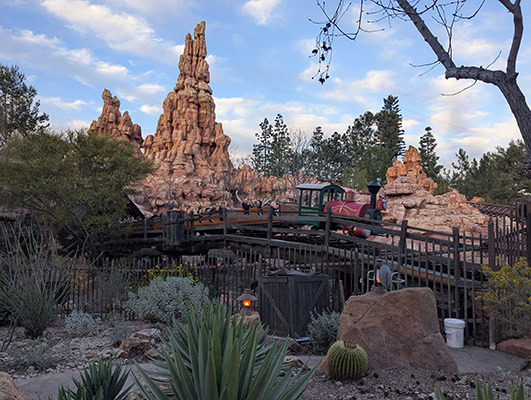 A rocky mountain soars above a railroad on roller coaster tracks