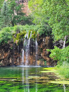 A small waterfall tumbles from a mossy clifftop to a vibrant green pool below